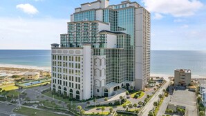 A multi-story hotel with a modern design, featuring a mix of glass and concrete facades, located near a beach with a clear view of the ocean.