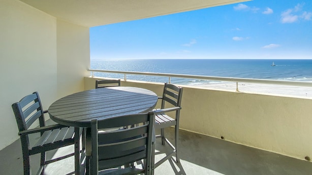 A balcony with a table and chairs, overlooking a beach with a clear view of the ocean and a distant boat. - Perdido Sun 904 (Pensacola)