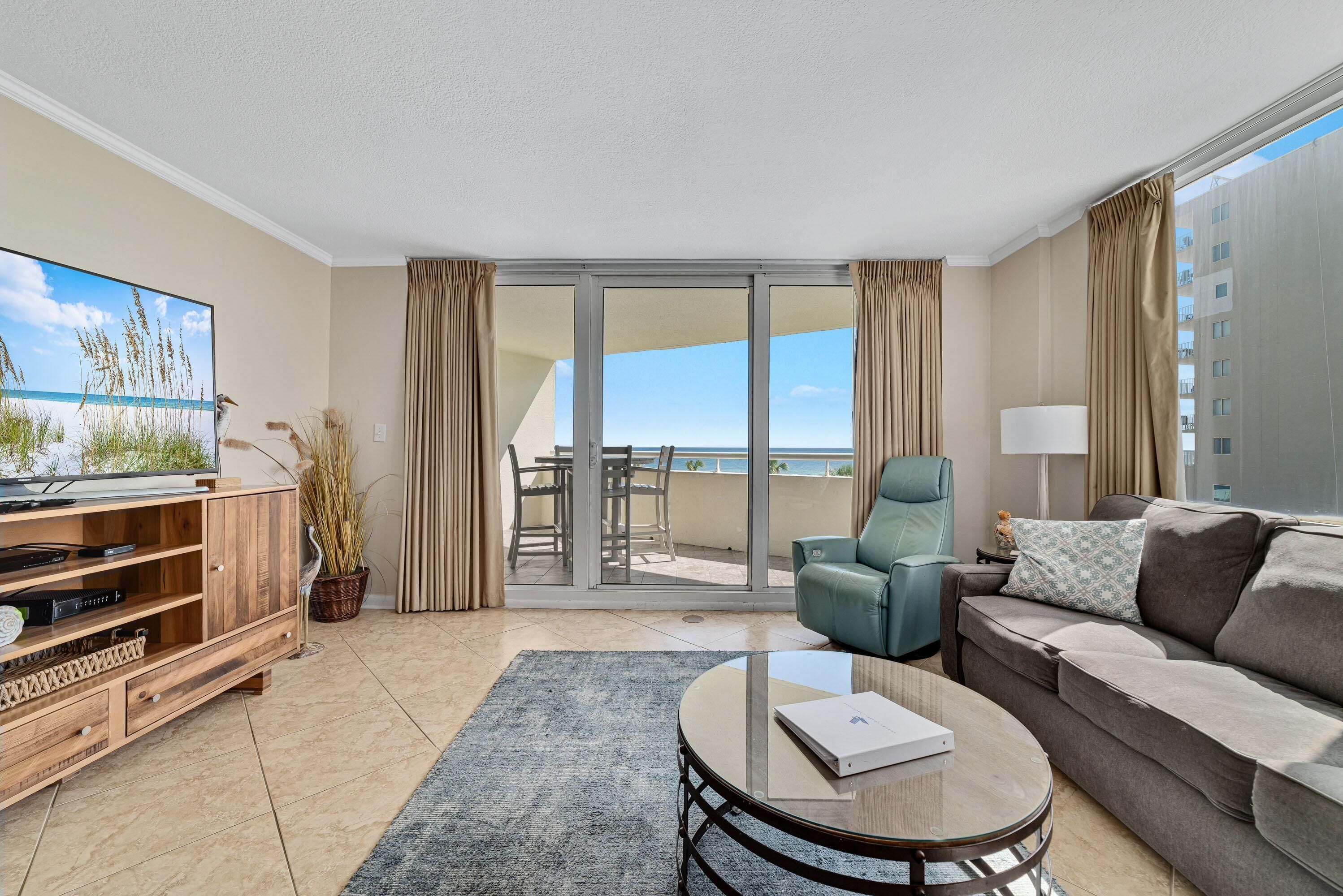 A modern hotel room with a large TV, a sofa, a coffee table, and a balcony with a view of the sea.