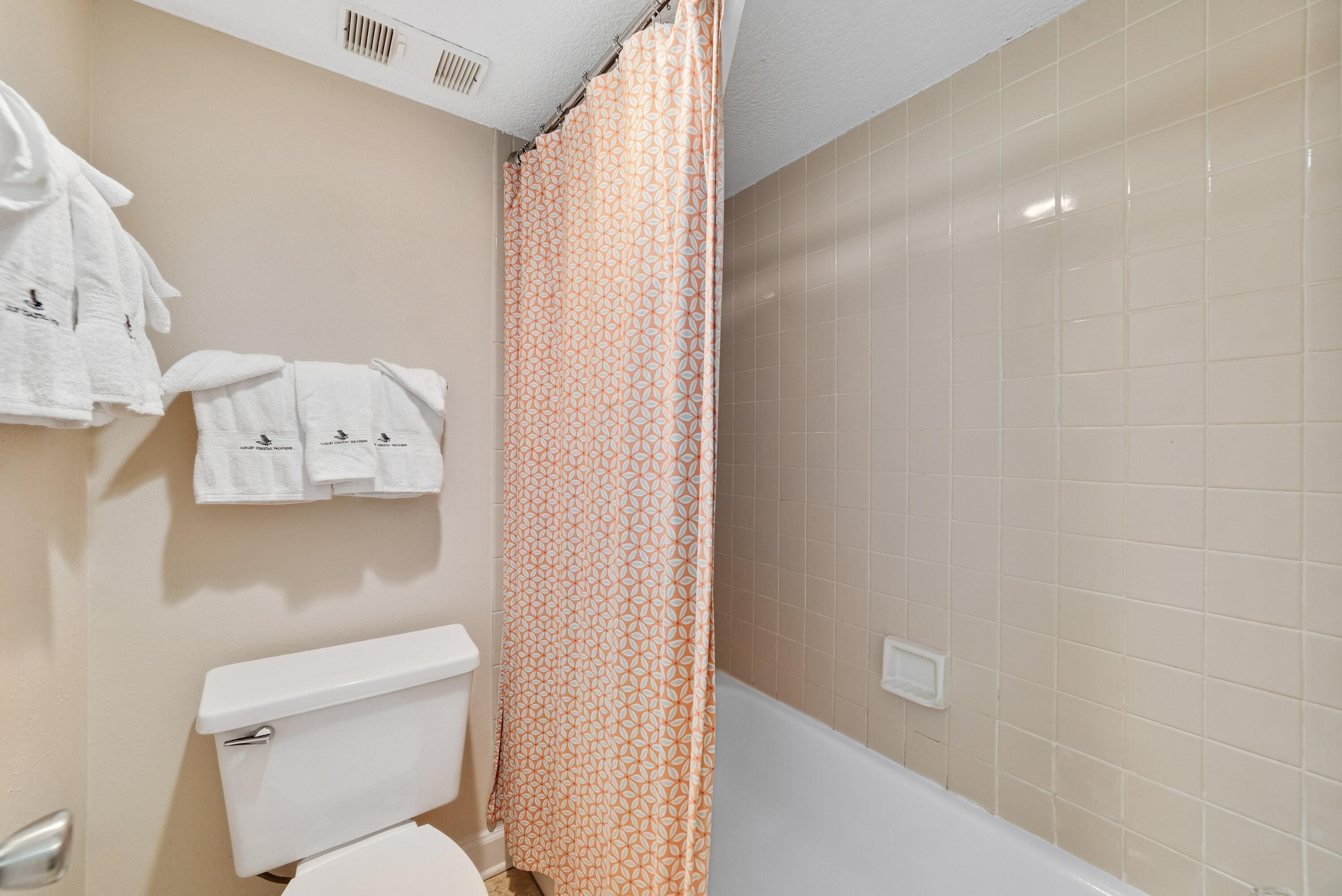 A bathroom with a toilet, a shower curtain, and a bathtub.