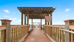 A wooden boardwalk leading to a covered area with a warning sign. - Beach Colony East 9C (Pensacola)