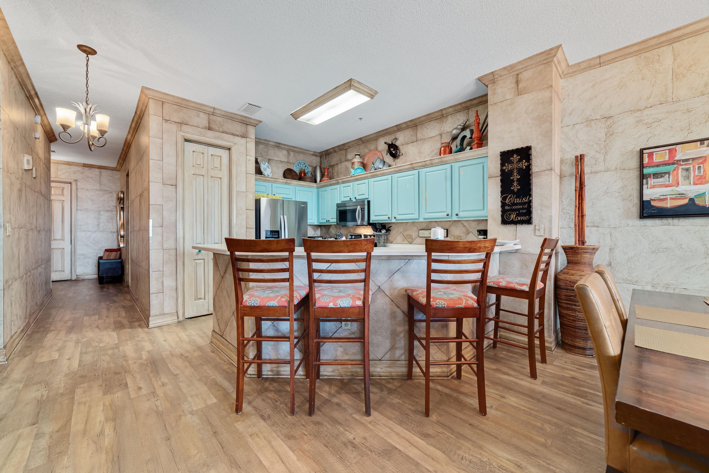 A kitchen with wooden flooring, a central island with bar stools, light blue cabinets, and a chandelier.