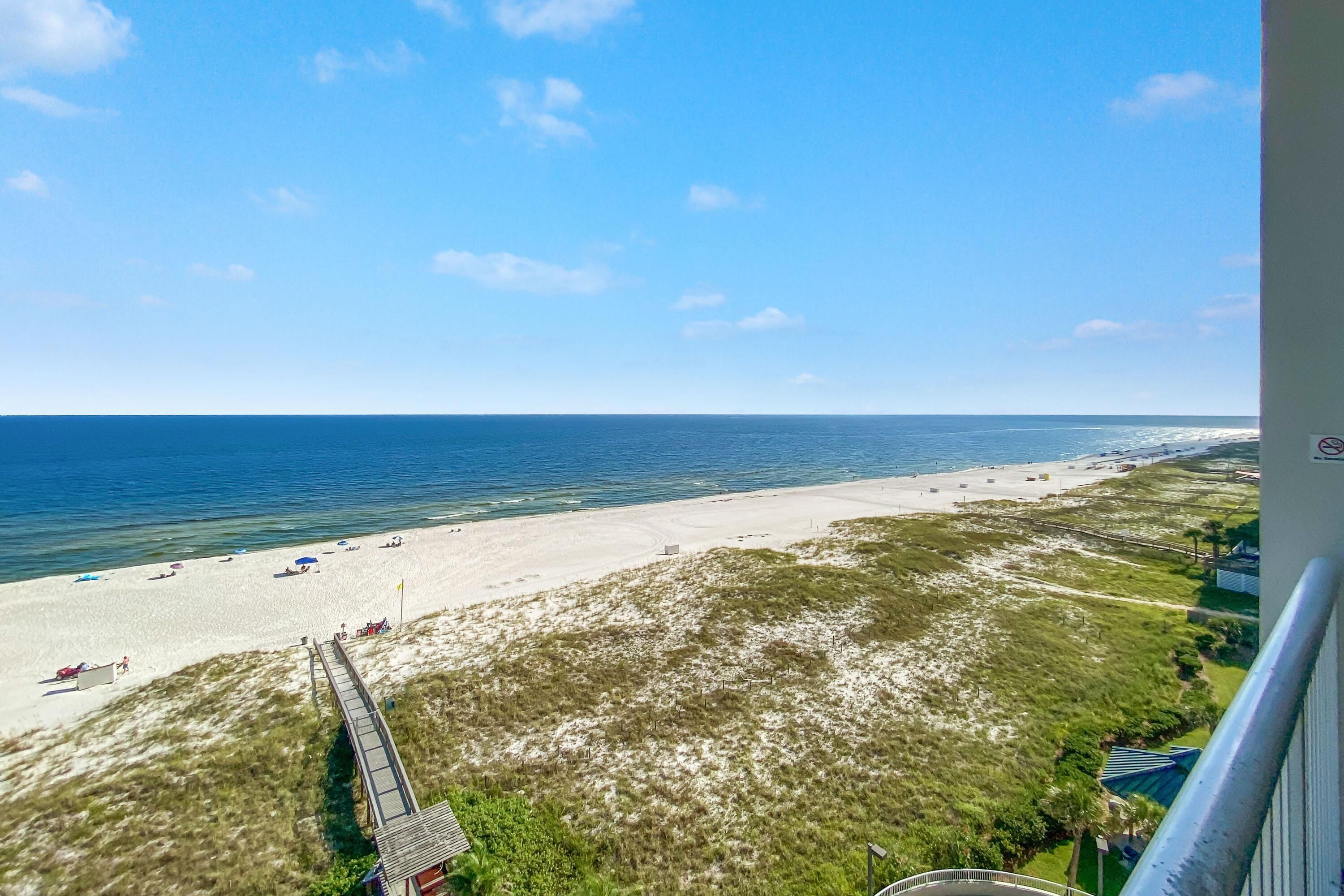 Ein Strand mit klarem Himmel, sandigem Ufer und einer Holzpromenade, die zum Strand führt.