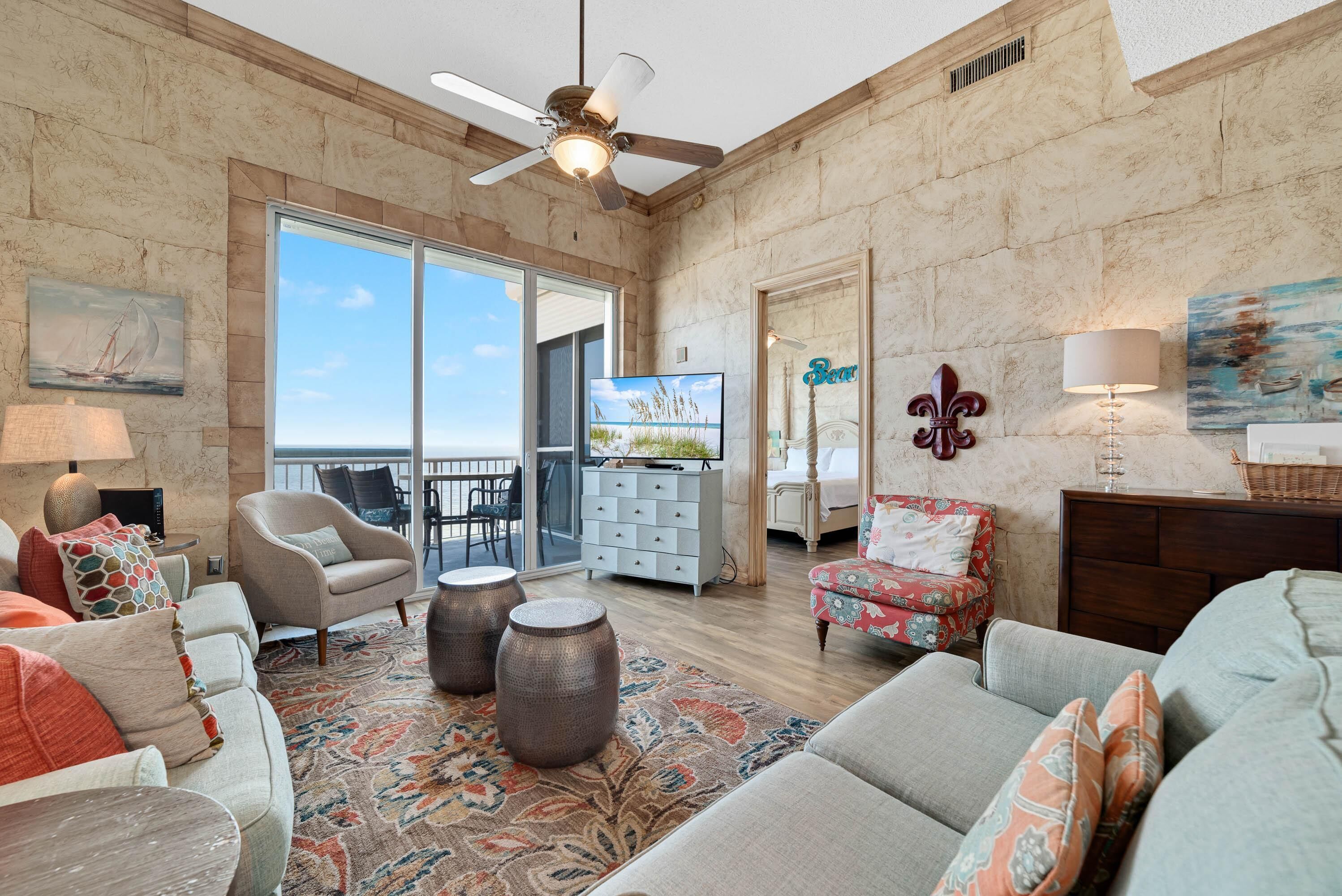 A spacious living room with a large window, a ceiling fan, and a television.