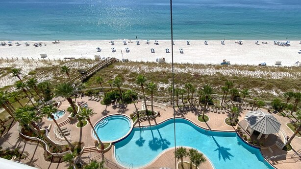 Een resort met een zwembad, strand en palmbomen.