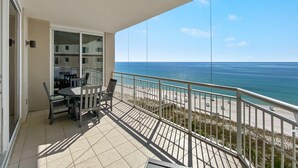 Een balkon met een tafel en stoelen, met uitzicht op een strand en zee.