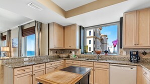 A modern kitchen with wooden cabinets, a granite countertop, and a built-in dishwasher. - Indigo East 1906 (Pensacola)