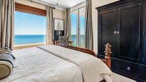 A bedroom with a large bed, a wardrobe, a chair, and a view of the sea. - Indigo East 1906 (Pensacola)