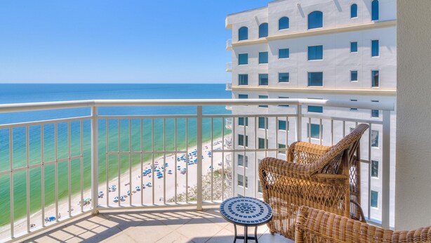 A balcony with a view of the beach and ocean, wicker furniture, and a tiled floor. - Indigo East 1906 (Pensacola)