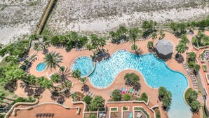 An aerial view of a resort with multiple swimming pools, a beach area with umbrellas, and a dock. - Indigo East 1906 (Pensacola)