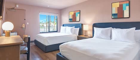 Habitación de hotel con dos camas, un escritorio, una silla y una ventana con vistas a palmeras, además de arte abstracto en la pared.
