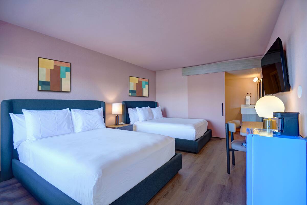 A hotel room with two beds, a desk, a chair, and artwork on the walls.