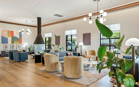 A spacious lounge area with a high ceiling, modern furniture, and large windows providing natural light.