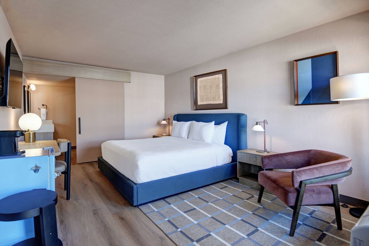 A hotel room with a bed, a desk, a chair, and a nightstand.