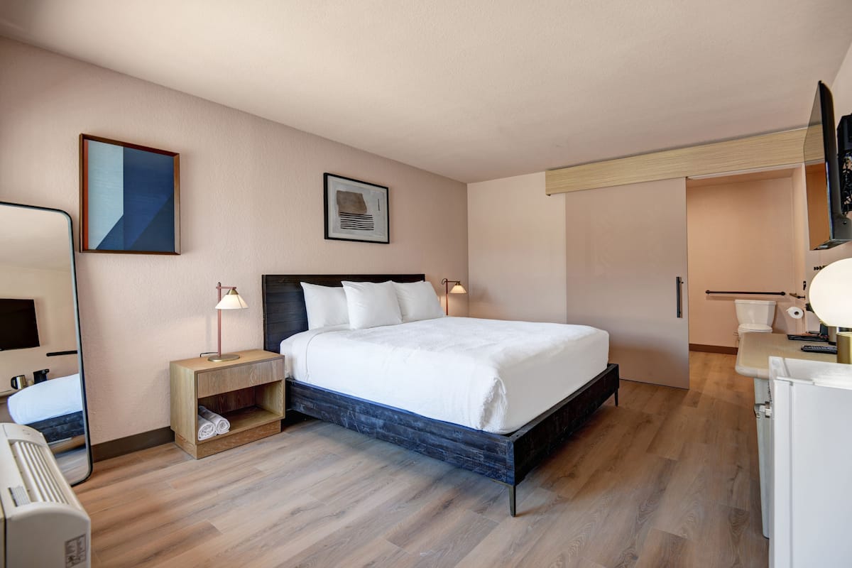 A modern hotel room with a large bed, bedside tables, a wardrobe, a mirror, and a television.