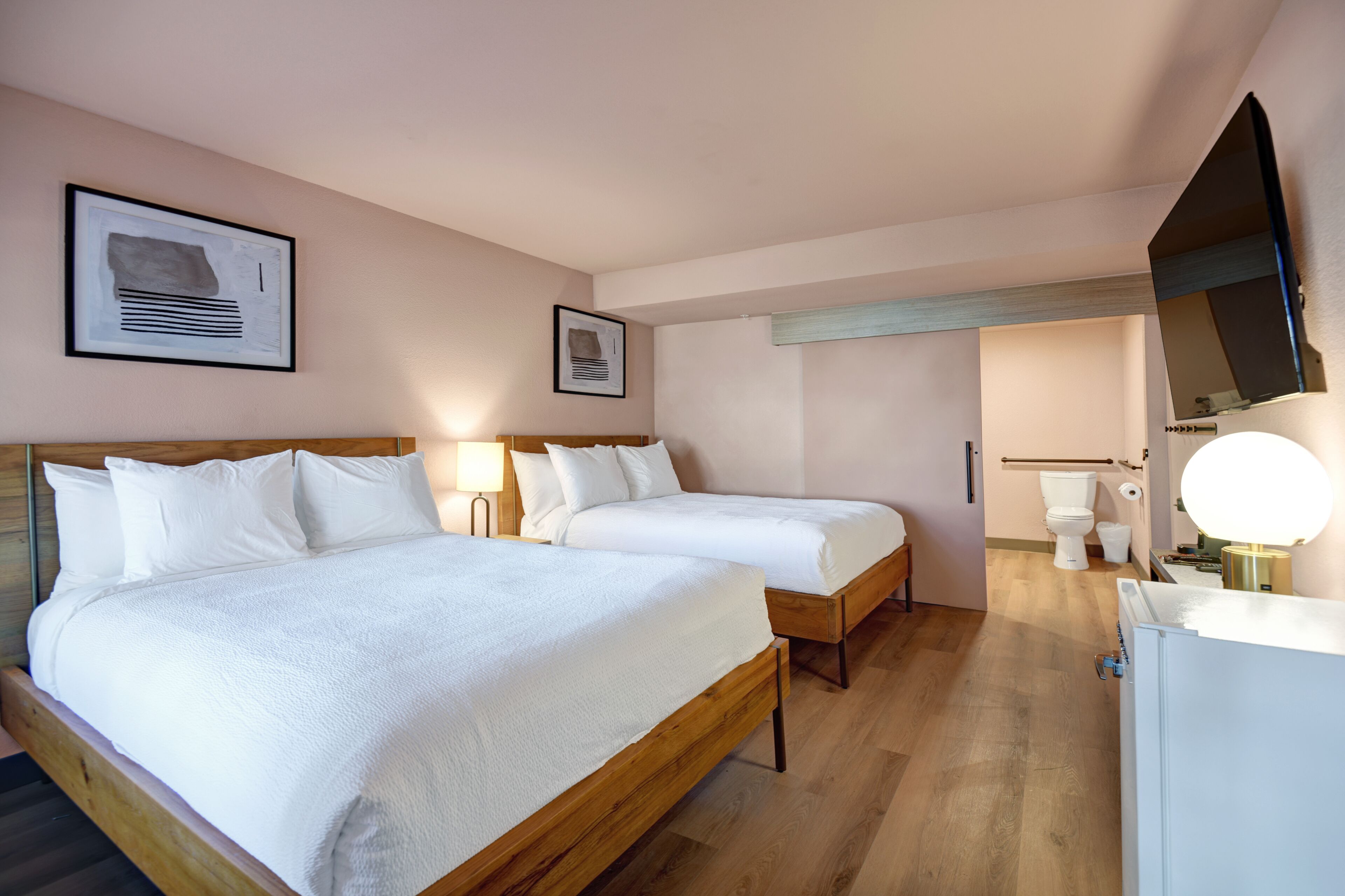 A hotel room with two beds, a wooden headboard, a large mirror, a toilet, and a sink.