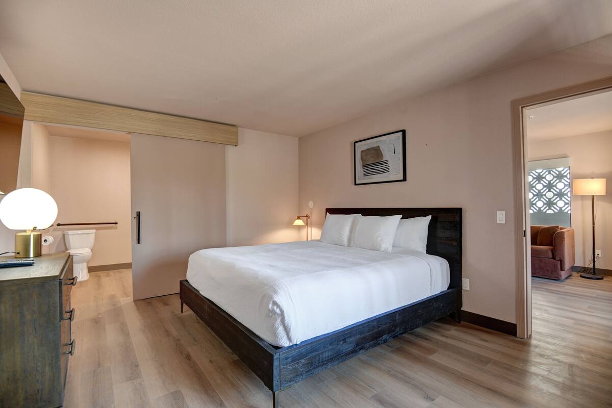 A bedroom with a wooden bed, a bedside table, a lamp, and a framed picture on the wall.