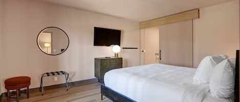 A bedroom with a bed, a round mirror, a bedside table with a lamp, a bench, and a wardrobe.