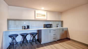 A modern kitchen with a microwave, coffee maker, and bar stools.