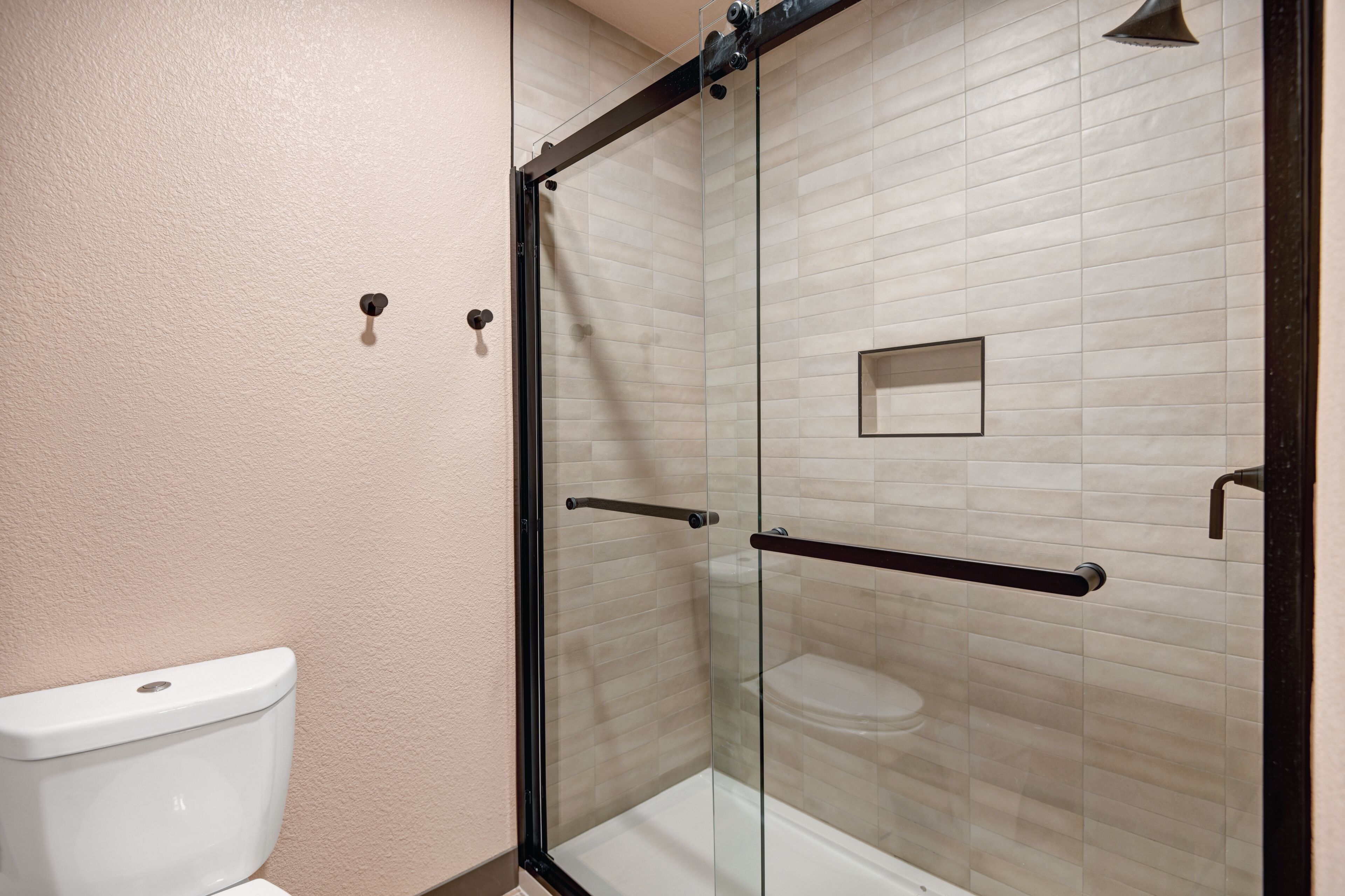 A glass-enclosed shower with a toilet visible through the glass, a towel rack, and a small rectangular mirror.