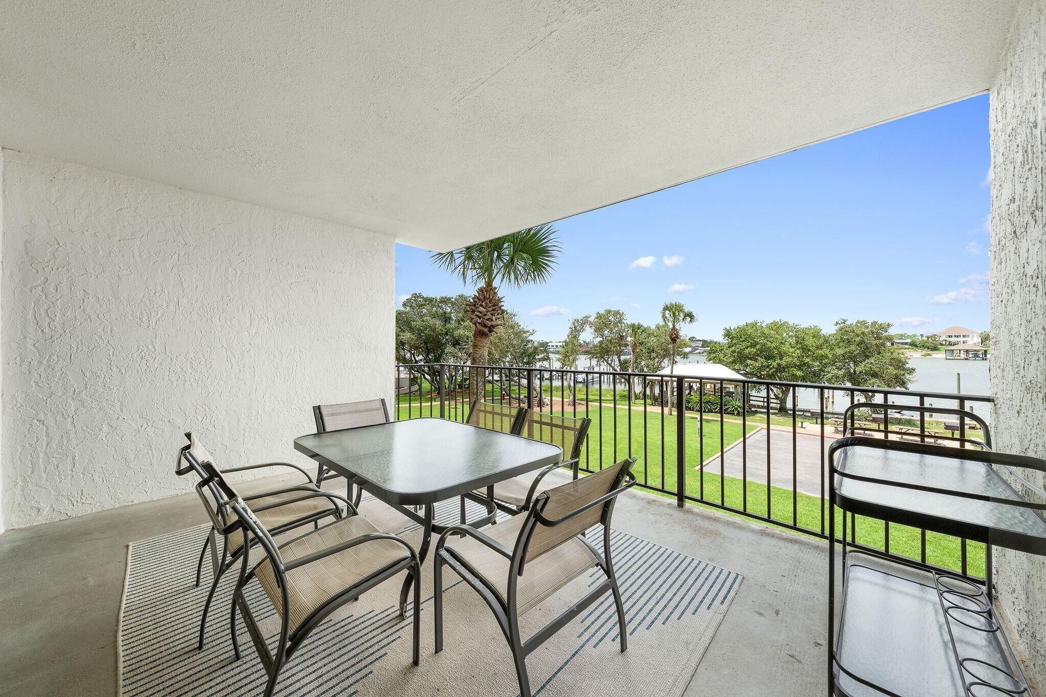 A balcony with a table and chairs, a view of a park, and a railing.