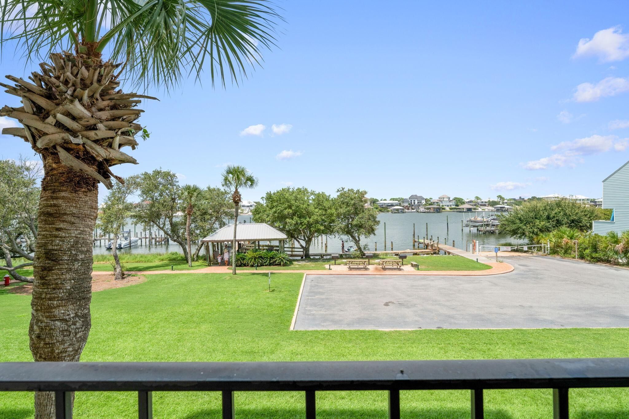 A grassy area with a palm tree, a gazebo, and a dock extending into a body of water.