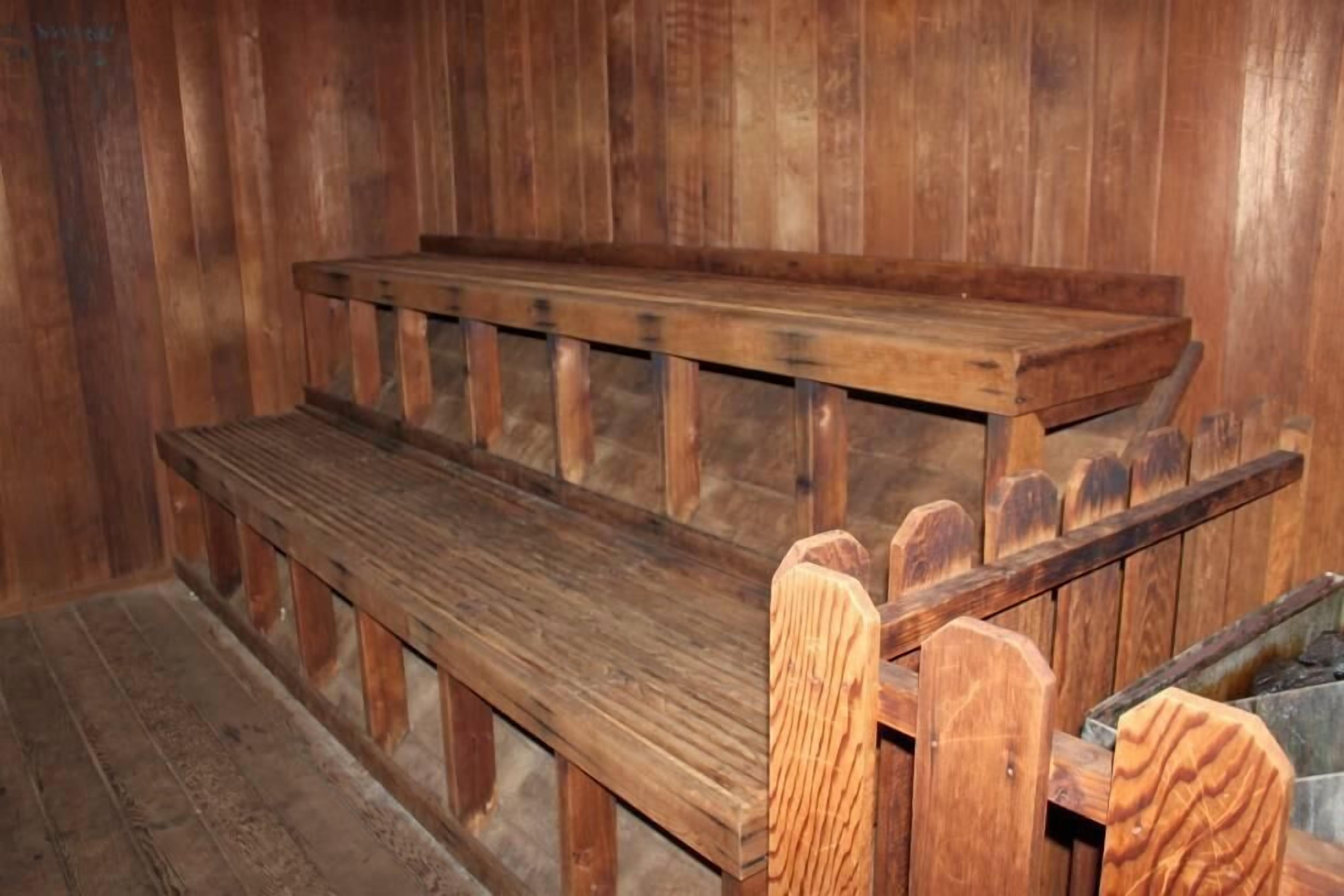 A wooden bench with a slatted backrest and a flat seat, positioned against a wooden wall.