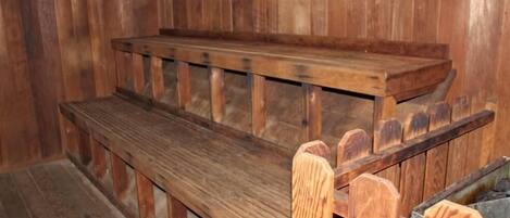A wooden bench with a slatted backrest and a flat seat, positioned against a wooden wall.