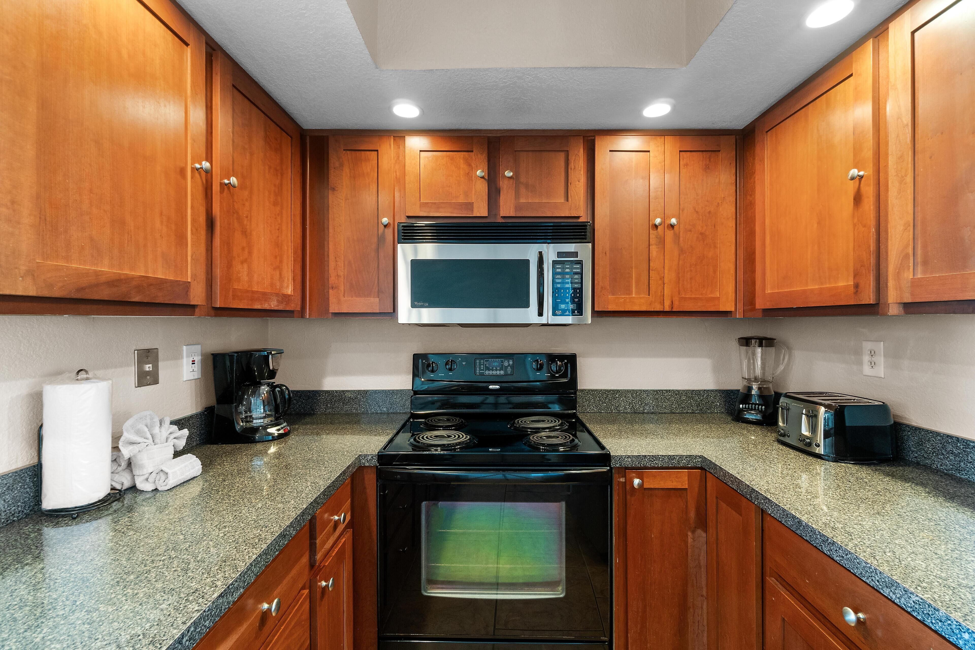 A kitchen with wooden cabinets, a stainless steel microwave, a black stove, a toaster, and a blender.