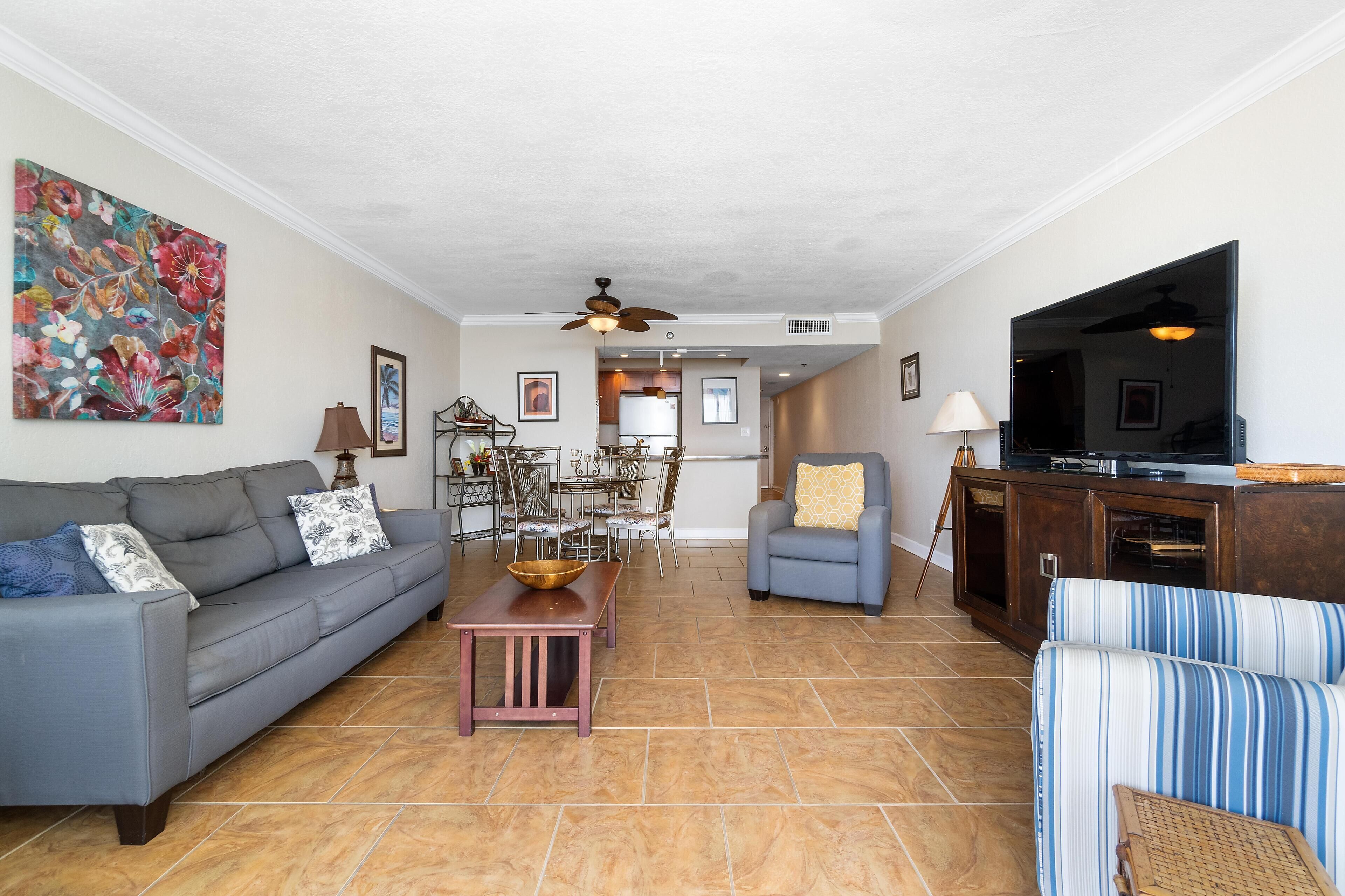 A living room with a sofa, armchairs, a TV, and a dining area with chairs and a table.