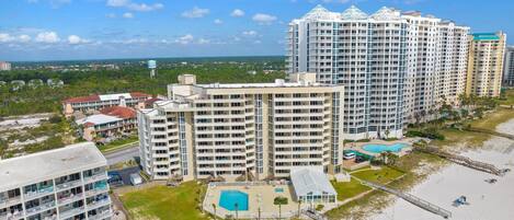 A high-rise hotel with multiple balconies, a swimming pool, and a beach area.