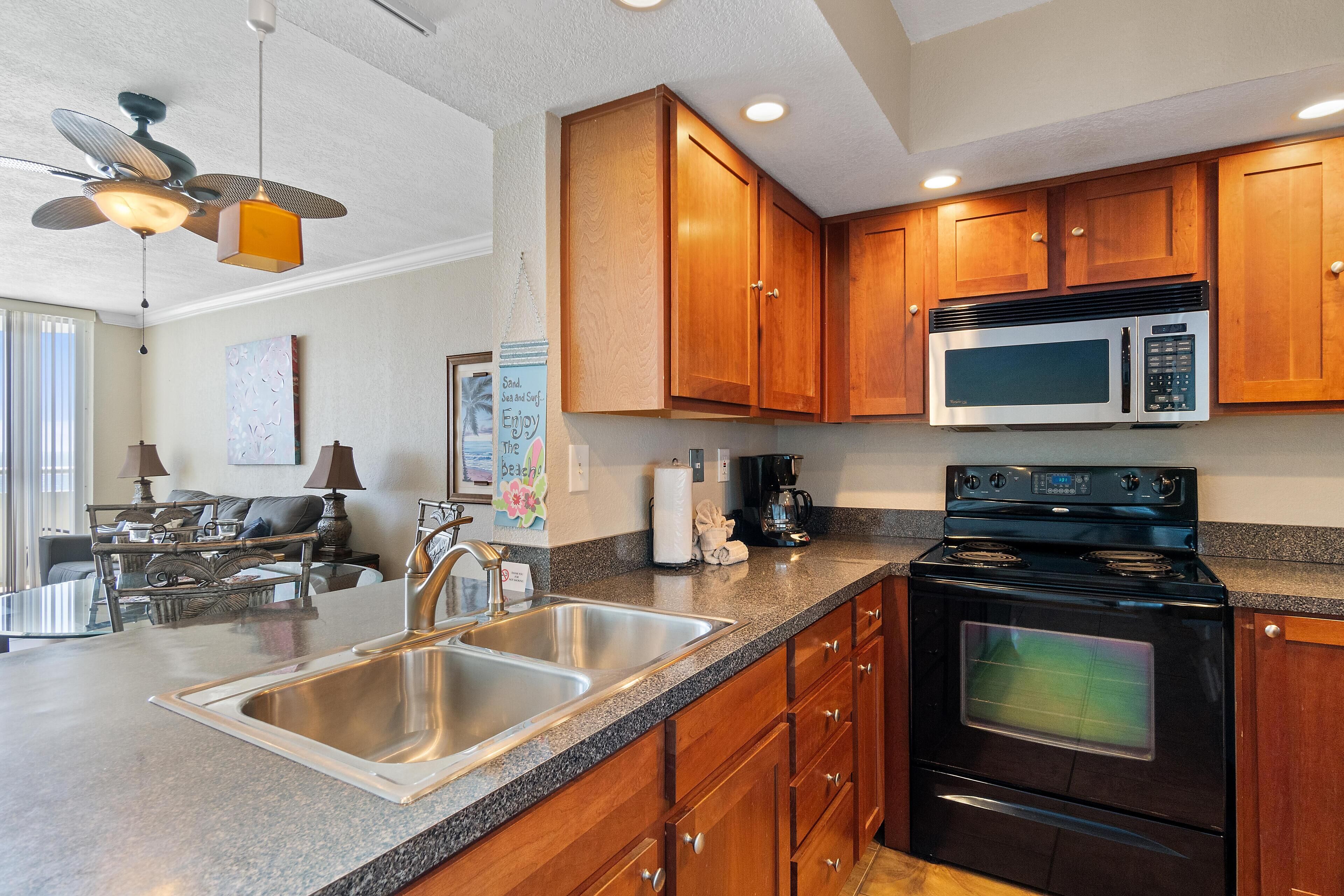 A kitchen with wooden cabinets, a stainless steel sink, a microwave, and a stove.