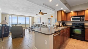 A modern kitchen with a large island, wooden cabinets, and a built-in microwave.
