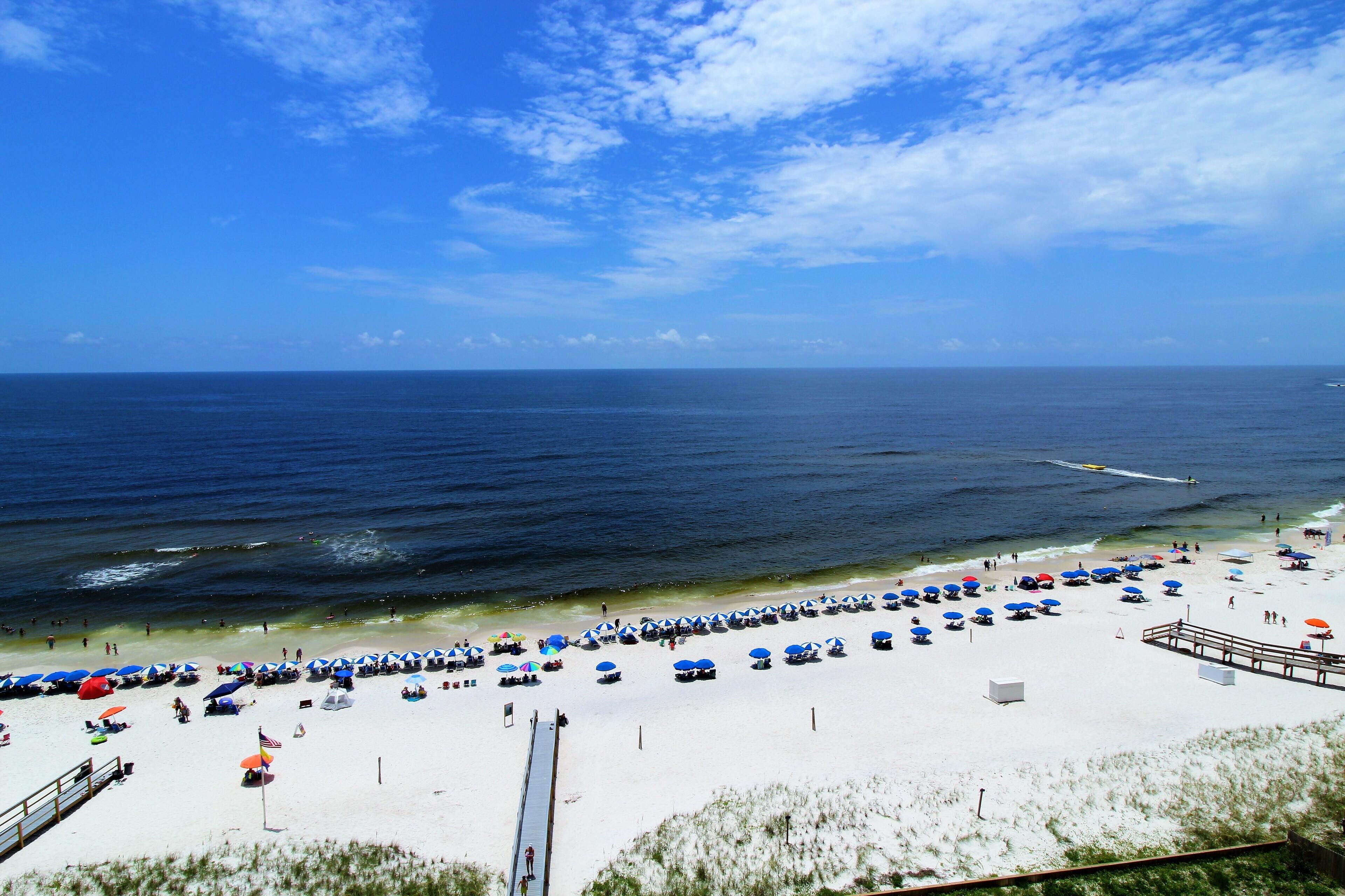 A beach with rows of umbrellas and beach chairs, a pier, and a clear view of the ocean.