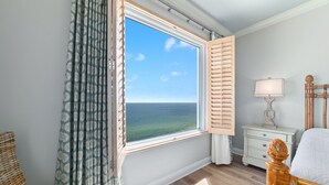 Ein Zimmer mit großem Fenster, einem Nachttisch mit Lampe und einem Sessel.