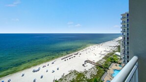 Blick auf einen Strand vom Balkon, mit Sonnenschirmen und einem Schwimmbecken.