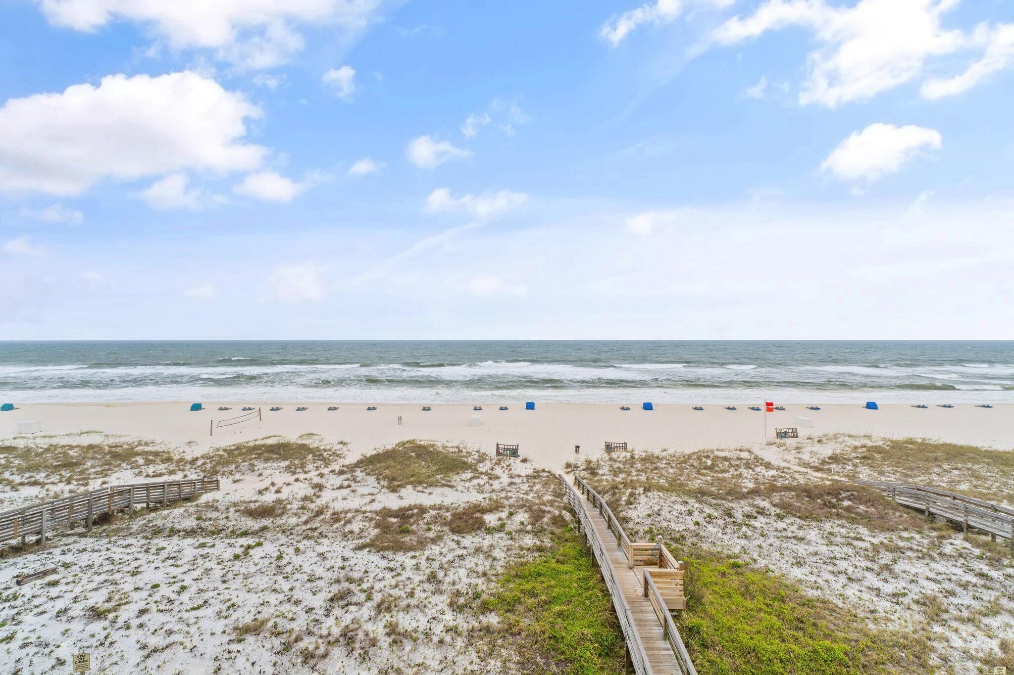 A beach with a wooden boardwalk leading to the shore, sandy beach, and ocean view.