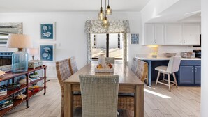 A dining area with a wooden table, wicker chairs, and a chandelier. - Shipwatch A504 (Pensacola)