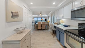 A modern kitchen with white cabinetry, a large stove, and a dining area with wicker chairs. - Shipwatch A504 (Pensacola)