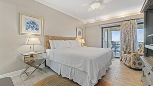 A bedroom with a bed, two bedside tables, a ceiling fan, and a view of the outdoors. - Shipwatch A504 (Pensacola)