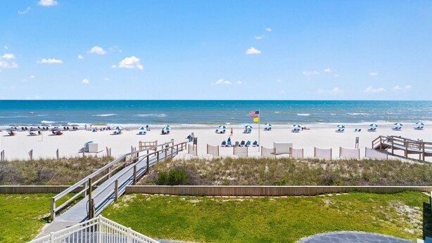 A beach with a wooden walkway leading to the shore, beach chairs, umbrellas, and a flag. - Perdido Sun 200 (Pensacola)