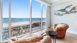 Une pièce dotée d’une grande fenêtre donnant sur une plage, d’un fauteuil en cuir, d’une petite table et d’un élément décoratif fixé au mur.