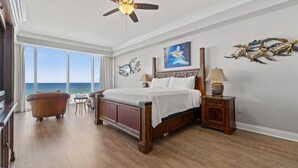 Une chambre spacieuse avec un grand lit, un ventilateur de plafond, une vue sur l’océan et un plancher en bois.