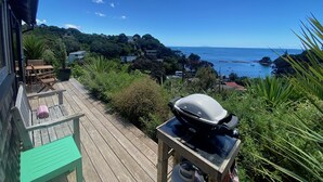 A wooden deck with a grill and a gas stove, overlooking a coastal area with houses and a clear blue sky.
