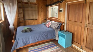 A wooden cabin bedroom with a bed, a nightstand, a window, a wardrobe, and a mosquito net.