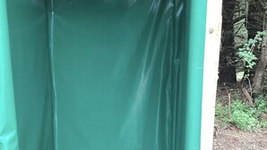 A small, enclosed space with a green tarp covering the walls and floor, a white pipe, and a wooden structure above. - Farmstay Glamping AGRItourism retreat-HERSHEYS HUT-cows, chicks, goat, minihorse (Tallahassee)