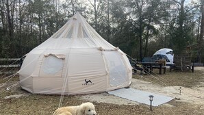 A large, dome-shaped tent with a logo on the side, surrounded by trees and a wooden deck with benches. - Farmstay Glamping AGRItourism retreat-HERSHEYS HUT-cows, chicks, goat, minihorse (Tallahassee)