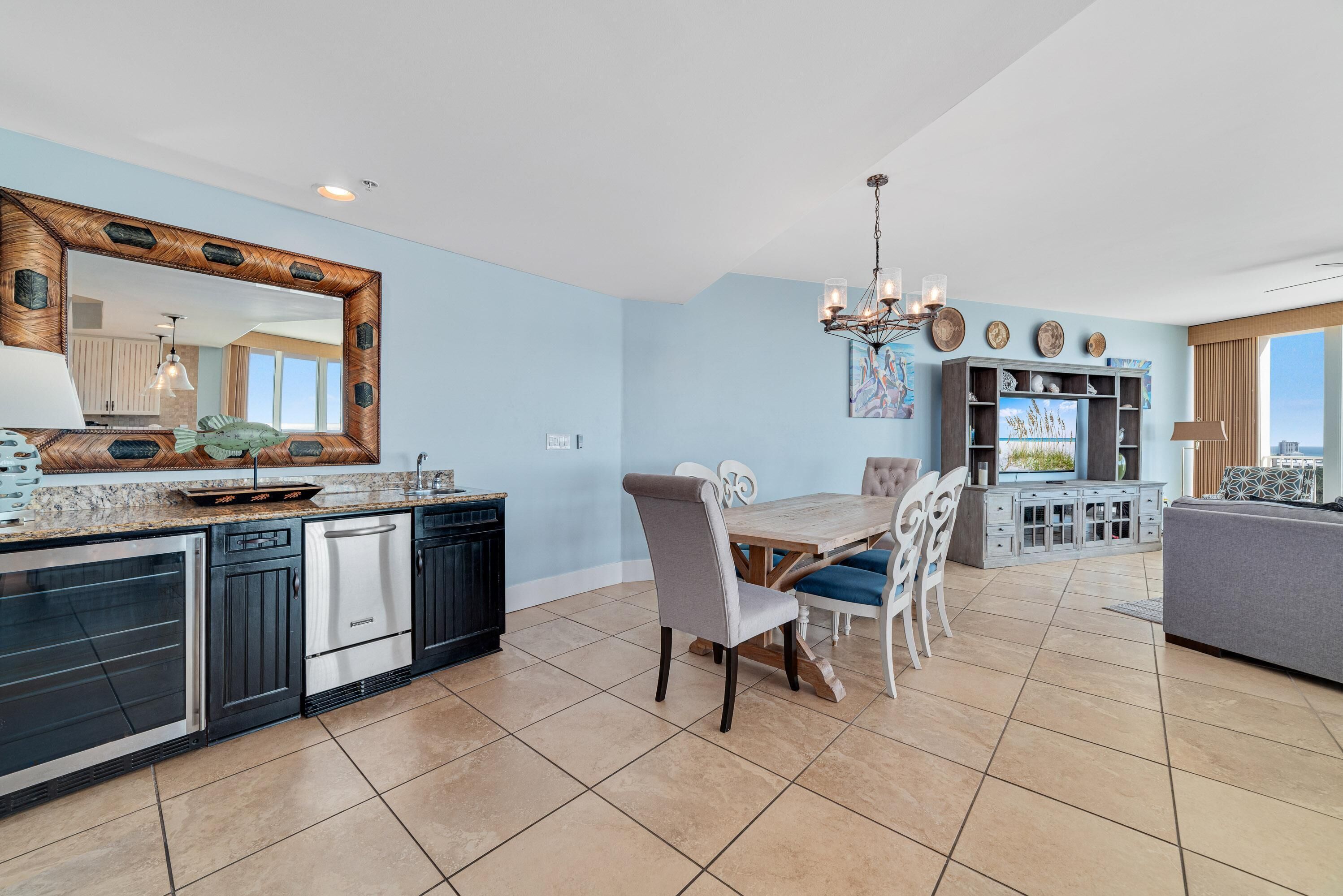 A modern kitchen with a large island, dining area with a wooden table and chairs, and a living room with a sofa and entertainment unit.