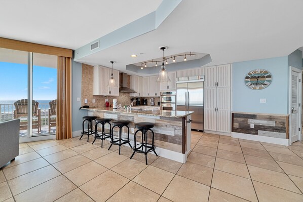 A modern kitchen with a large island, bar stools, and a view of the city. - Caribe D1110 (Orange Beach)