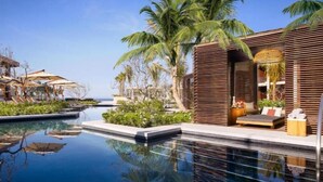 Un resort moderno con piscina cristalina, palmeras y una estructura de madera con zona de estar.